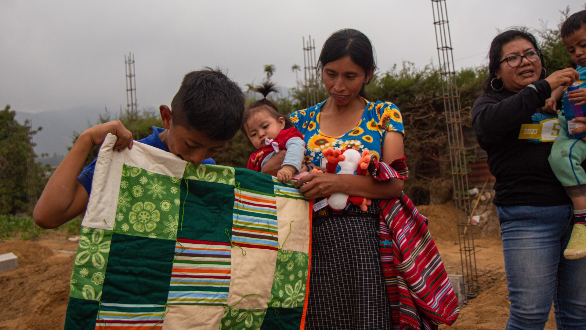 Guatemalan boy and mother holding a baby admire a handmade quilt