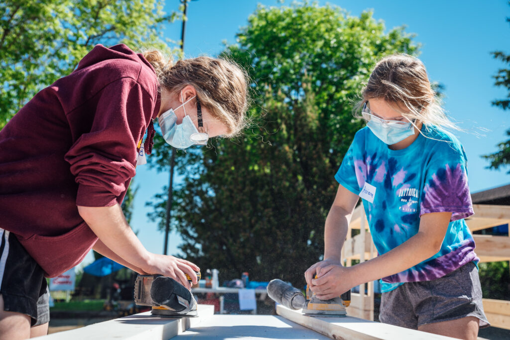 Two teenage girls sanding lumber